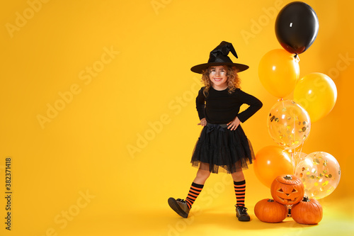 Fotótapéta Cute little girl with pumpkins and balloons wearing Halloween costume on yellow background
