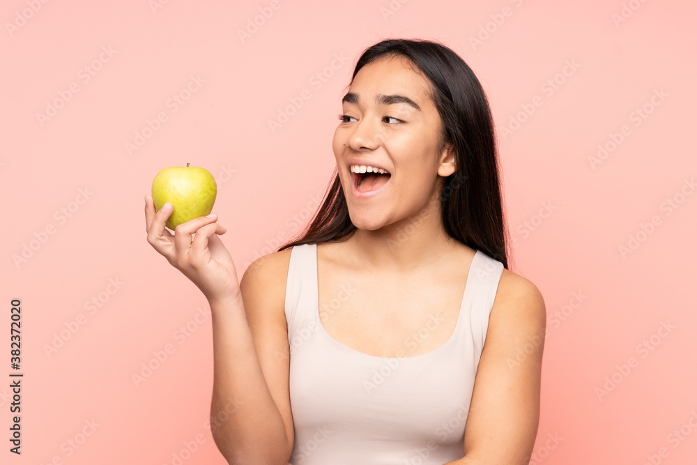 Young Indian woman isolated on pink background with an apple and happy Young Indian woman isolated on pink background with an apple and happy
