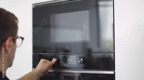 Close up of young man setting microwave oven timer warming food in modern kitchen.