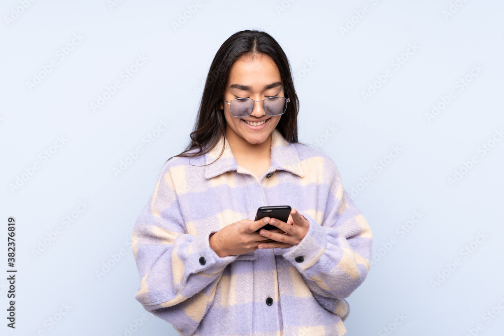 Young Indian woman isolated on blue background sending a message with the mobile Young Indian woman isolated on blue background sending a message with the mobile