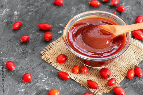 Homemade rosehip marmalade in glass bowl with fresh rose hip fruits on rustic background ( rosa canina )