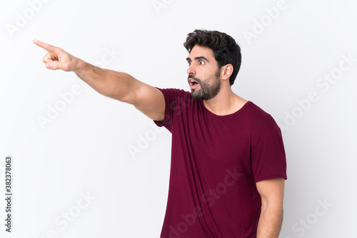 Young handsome man with beard over isolated white background pointing away