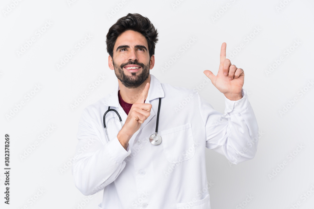 Young handsome man with beard over isolated white background wearing a doctor gown and pointing up