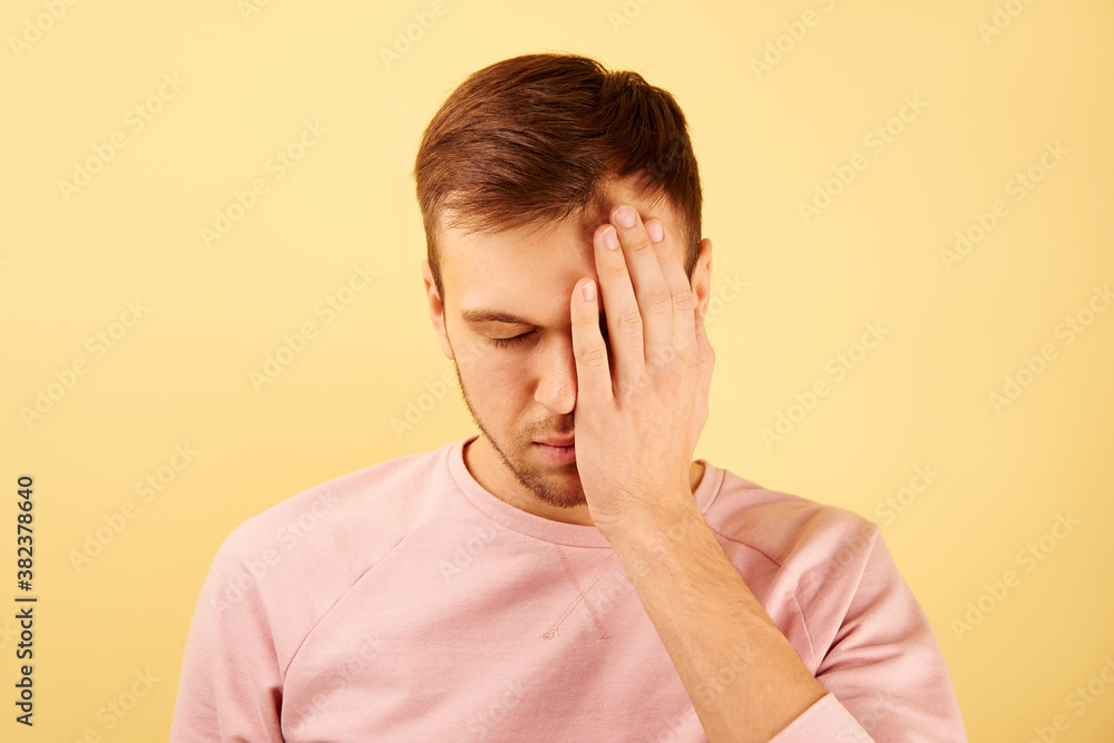 Man with closed eyes covers half of his face with hand on yellow background isolated, concept of headache, feeling of guilt and frustration Man with closed eyes covers half of his face with hand on yellow background isolated, concept of headache, feeling of guilt and frustration