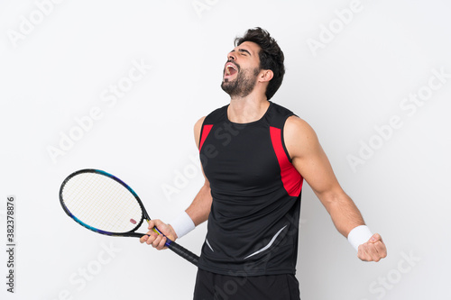 Young handsome man with beard over isolated white background playing tennis and celebrating a victory