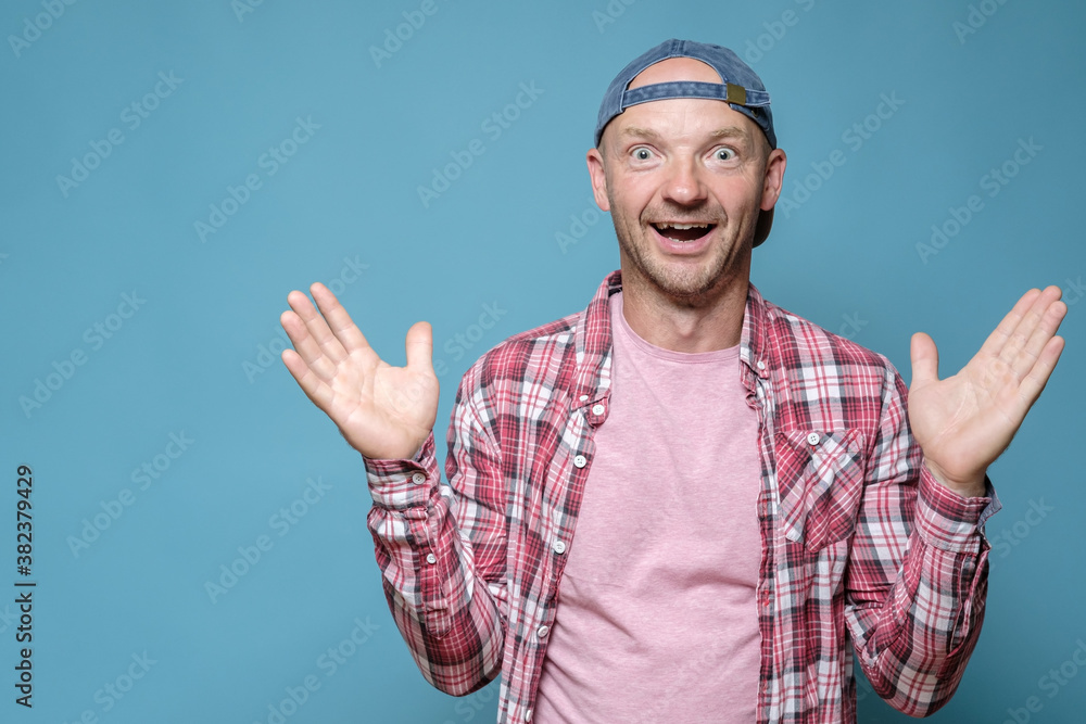 Funny man in a cap threw up hands in surprise, he is glad for a pleasant surprise, opened mouth in shock and looks with big eyes. 