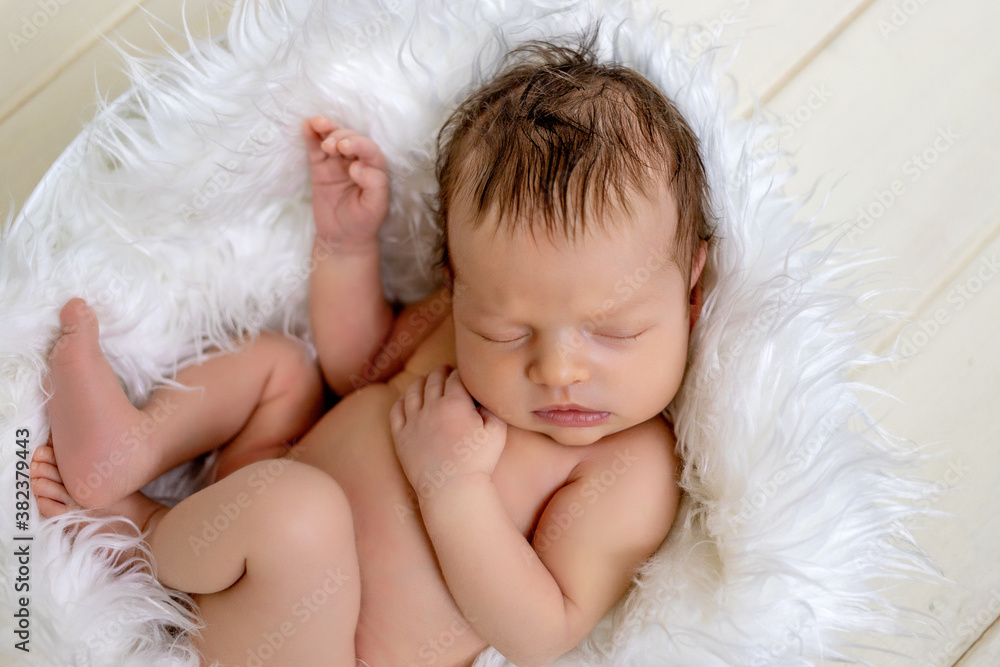 newborn baby girl two weeks sweetly sleeping in a basket with white fur on the background of a wooden floor newborn baby girl two weeks sweetly sleeping in a basket with white fur on the background of a wooden floor