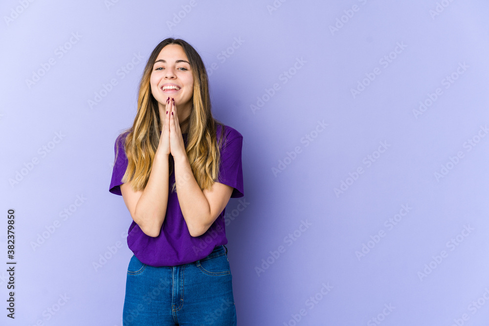 Young caucasian woman isolated on purple background holding hands in pray near mouth, feels confident. Young caucasian woman isolated on purple background holding hands in pray near mouth, feels confident.