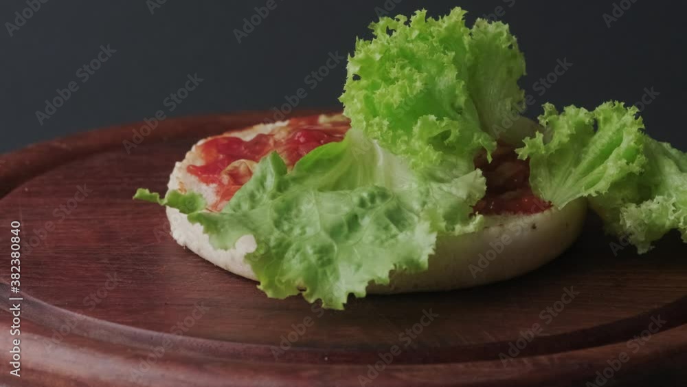 Lettuce falls on a bun covered with ketchup. Burger making process in slow motion. Lettuce falls on a bun covered with ketchup. Burger making process in slow motion.