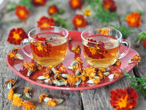 Alternative medicine. Tea cups with herbal tea with calendula flowers or Chernobrivtsi or Mary's Gold on a red plate on a vintage wooden background with dried flowers. Herbal tea benefits your health.