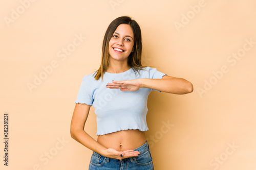 Young woman isolated on beige background holding something with both hands, product presentation.