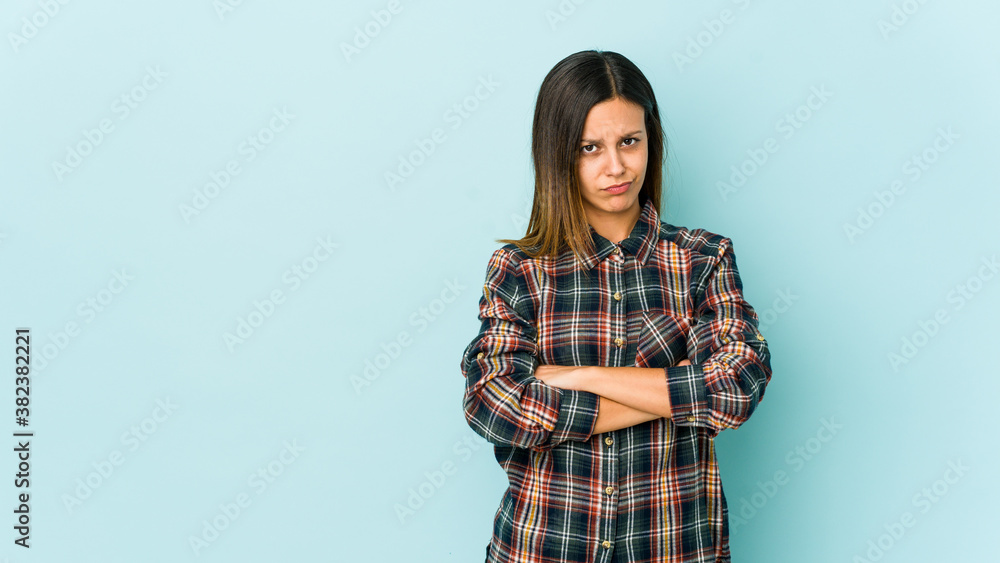 Young woman isolated on blue background frowning face in displeasure, keeps arms folded. Young woman isolated on blue background frowning face in displeasure, keeps arms folded.