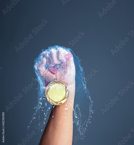 Winner raising hand with gold medal through water splash on dark grey background, closeup
