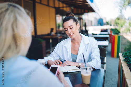 Positive woman speaking to coworker on summer terrace during coffee break