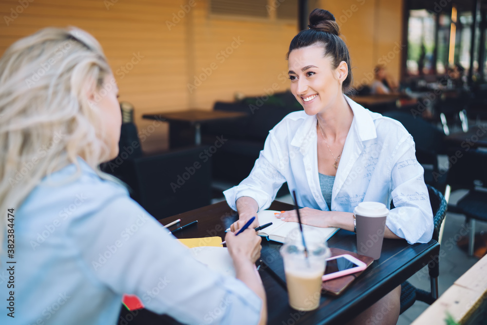 Fototapeta premium Smiling woman listening to colleague at table in cafe