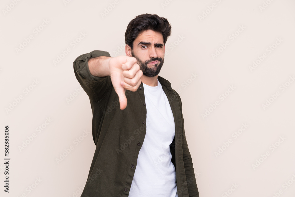 Young handsome man with beard over isolated background showing thumb down with negative expression Young handsome man with beard over isolated background showing thumb down with negative expression