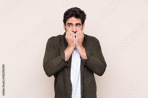 Young handsome man with beard over isolated background nervous and scared putting hands to mouth