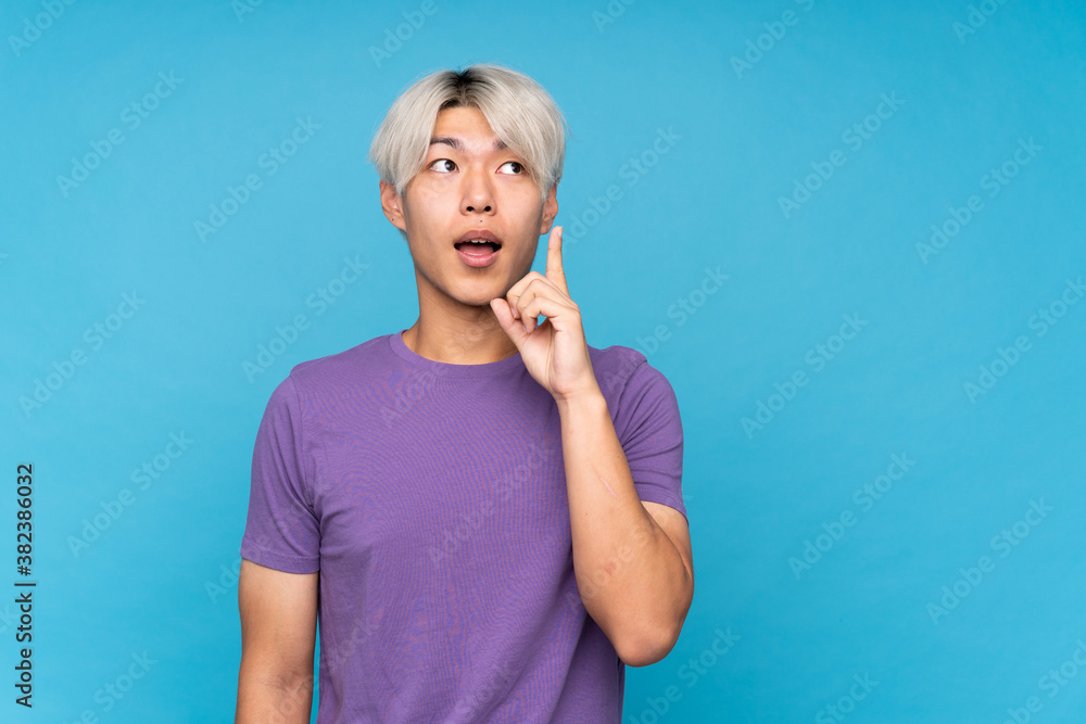 Young asian man over isolated blue background thinking an idea pointing the finger up Young asian man over isolated blue background thinking an idea pointing the finger up