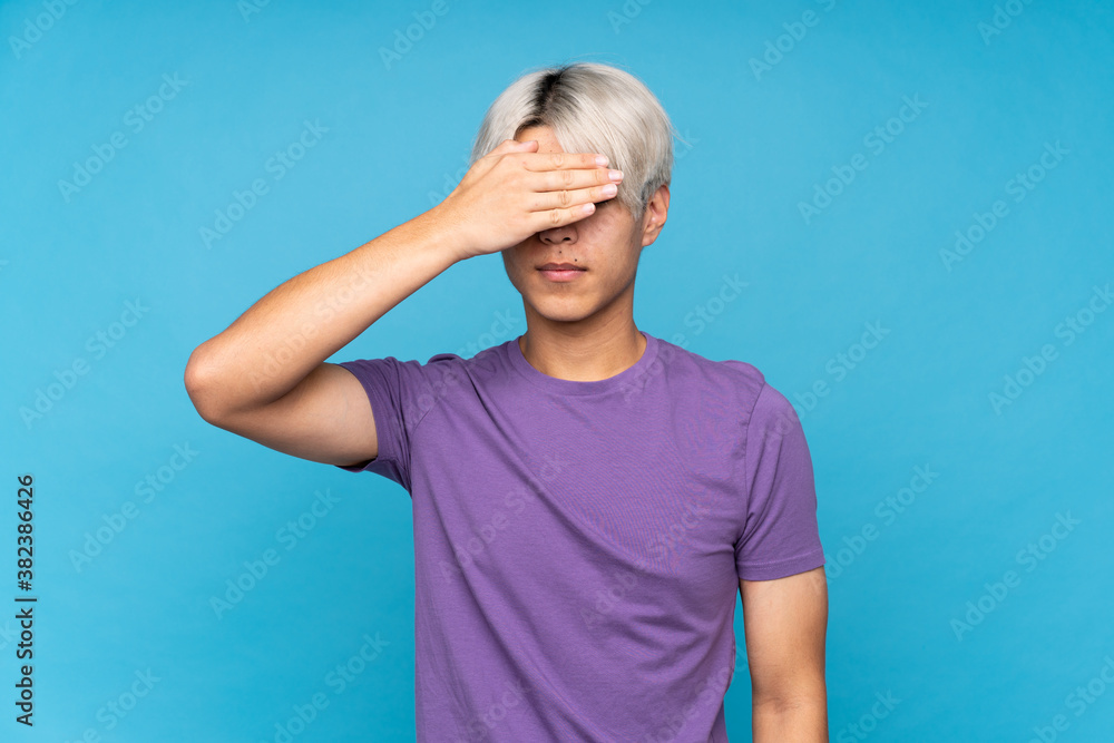 Young asian man over isolated blue background covering eyes by hands. Do not want to see something Young asian man over isolated blue background covering eyes by hands. Do not want to see something
