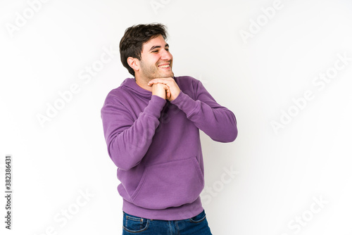 Young man isolated on white background keeps hands under chin, is looking happily aside.