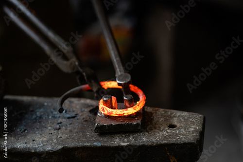 Blacksmith bends iron rod on the anvil with tool