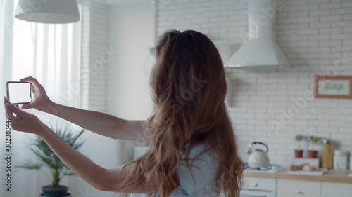 Beautiful girl posing to phone camera in kitchen interior. Woman making selfie.