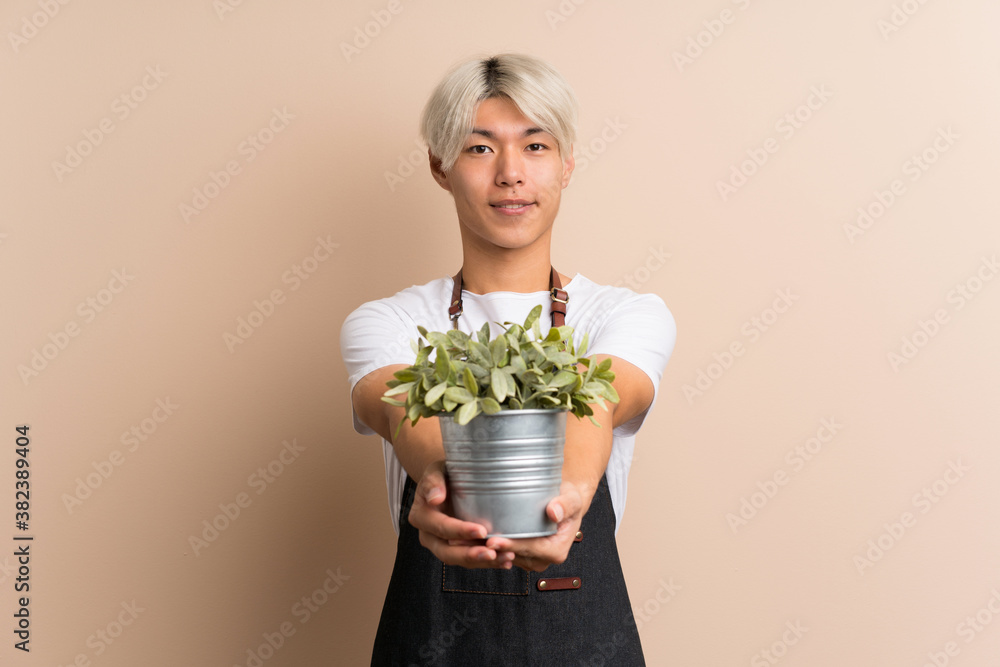 Young asian man over isolated background taking a flowerpot Young asian man over isolated background taking a flowerpot