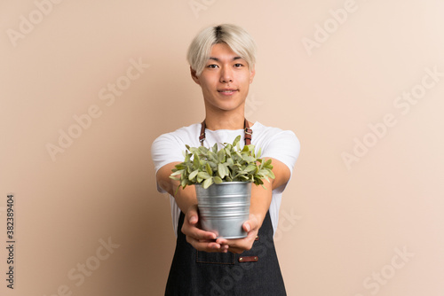 Young asian man over isolated background taking a flowerpot