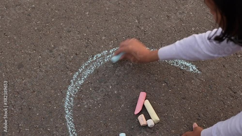 A woman drawing a rainbow with a chalk on asphalt. Drawings paintings on asphalt