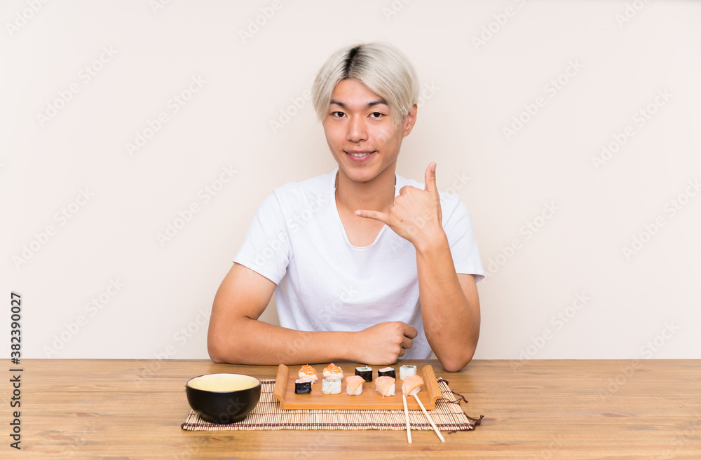 Young asian man with sushi in a table making phone gesture Young asian man with sushi in a table making phone gesture