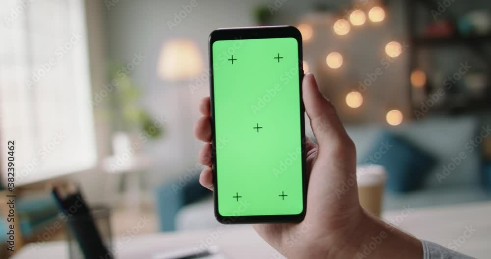 Hand of guys holding a smartphone with green chroma key screen in living room. Template for online store or social media 4k footage Hand of guys holding a smartphone with green chroma key screen in living room. Template for online store or social media 4k footage