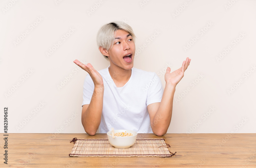 Young asian man with ramen in a table with surprise facial expression Young asian man with ramen in a table with surprise facial expression
