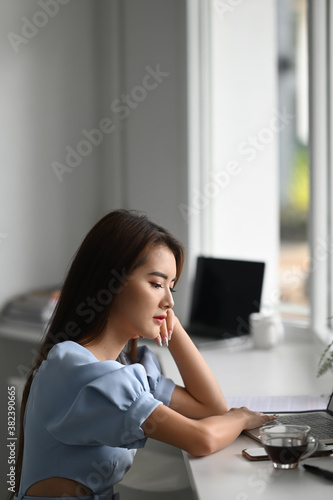 Portrait of female freelancer sitting in her office while looking at screen of laptop.
