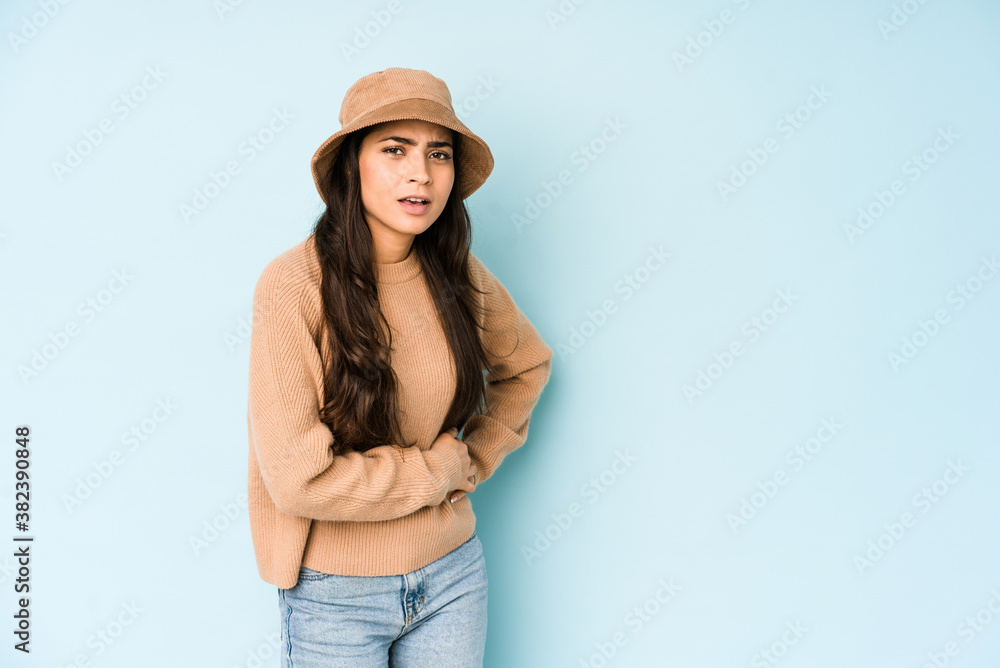 Young indian woman wearing a hat isolated on blue background having a liver pain, stomach ache. Young indian woman wearing a hat isolated on blue background having a liver pain, stomach ache.