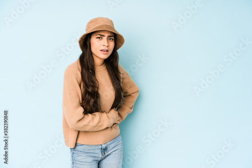 Young indian woman wearing a hat isolated on blue background having a liver pain, stomach ache.