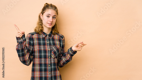 Young caucasian woman isolated on beige background pointing to different copy spaces, choosing one of them, showing with finger.