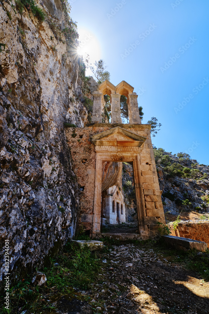 Ruins of abandoned Orthodox Katholiko monastery in Avlaki gorge, Akrotiri, Chania, Crete, Greece. Entrance gate. Upshot against sun. Spring daytime