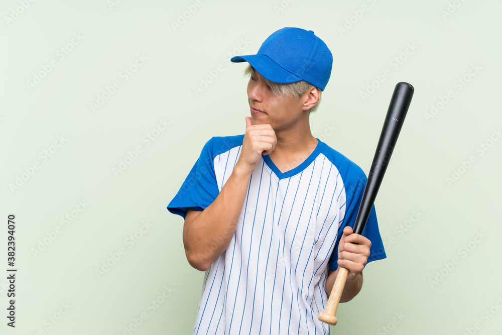 Young asian man playing baseball over isolated green background thinking an idea and looking side Young asian man playing baseball over isolated green background thinking an idea and looking side