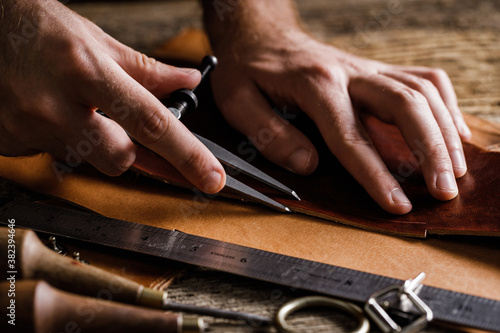 Close up of a shoemaker or artisan worker hands. Leather craft tools on old wood table. Leather craft workshop.