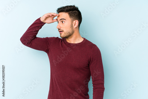 Young caucasian man isolated on blue background looking far away keeping hand on forehead.