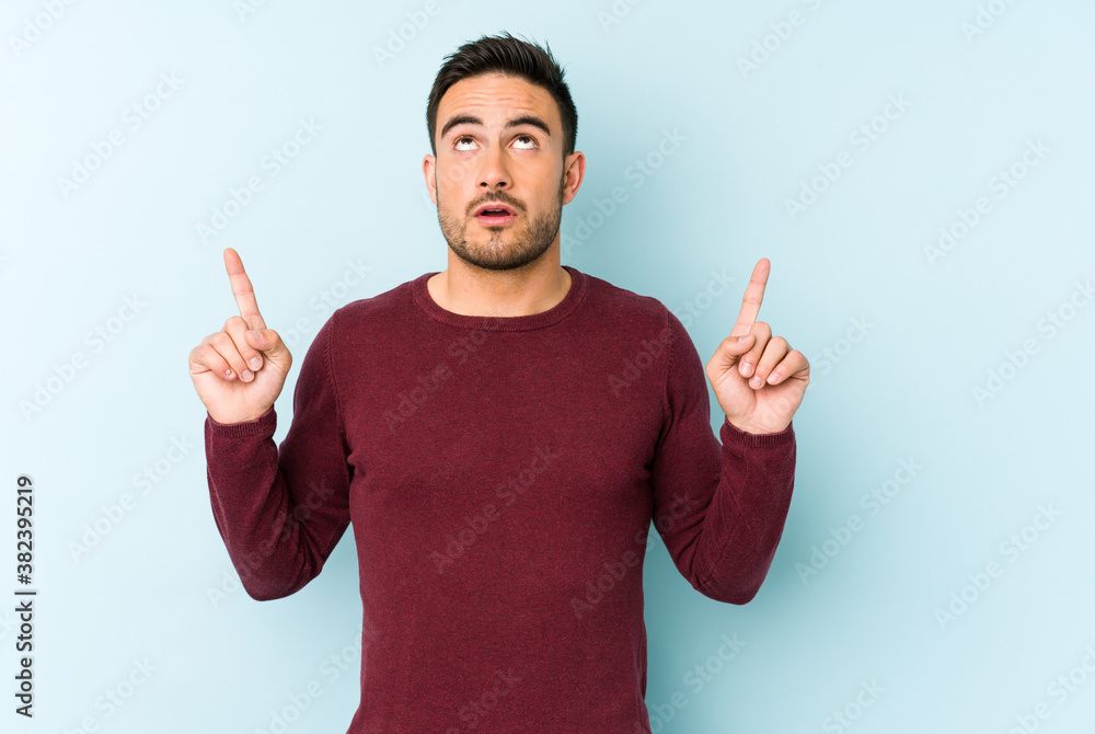 Young caucasian man isolated on blue background pointing upside with opened mouth. Young caucasian man isolated on blue background pointing upside with opened mouth.