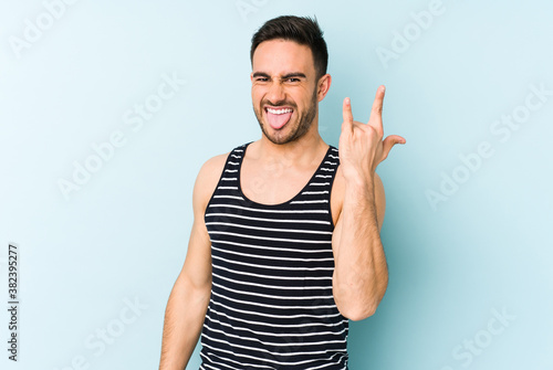 Young caucasian man isolated on blue background showing rock gesture with fingers