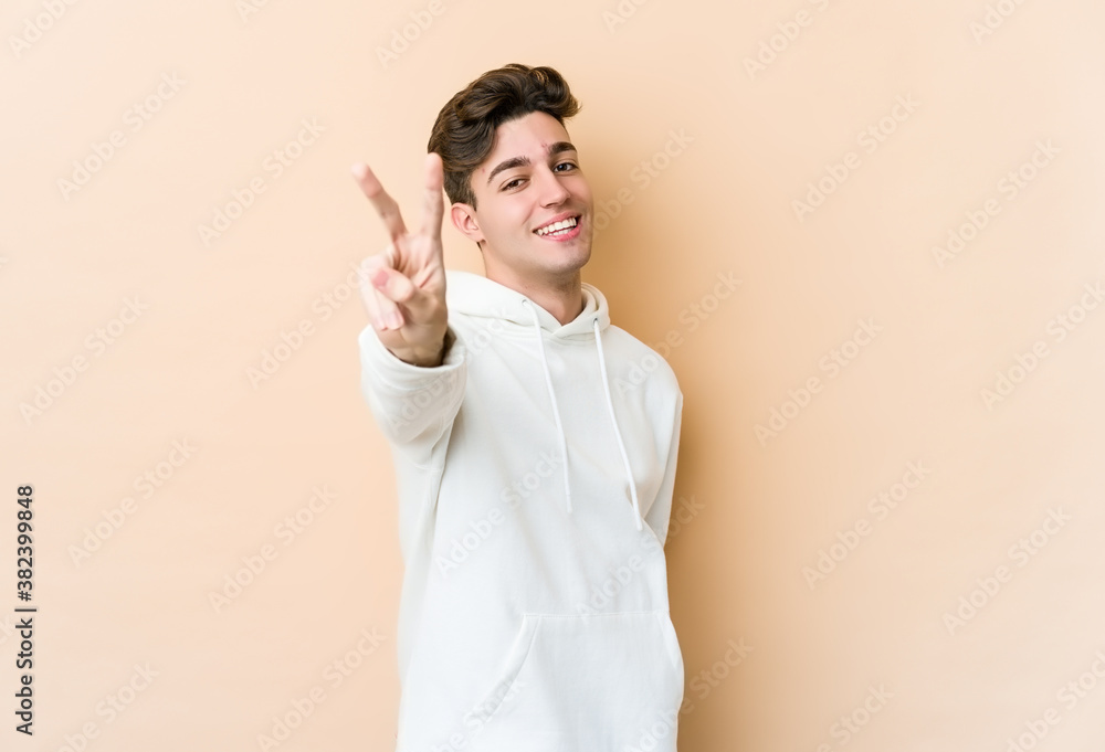 Young caucasian man isolated on beige background joyful and carefree showing a peace symbol with fingers. Young caucasian man isolated on beige background joyful and carefree showing a peace symbol with fingers.