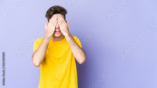 Young caucasian man isolated on purple background covers eyes with hands, smiles broadly waiting for a surprise.