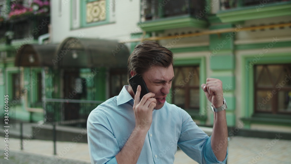 Happy businessman celebrating victory with mobile phone at street