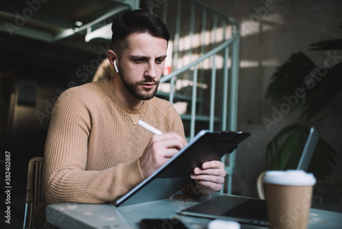 Man in beige sweater writing thoughts in notepad