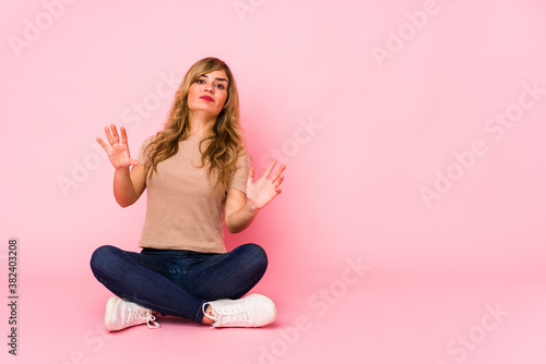 Young blonde caucasian woman sitting on a pink studio being shocked due to an imminent danger