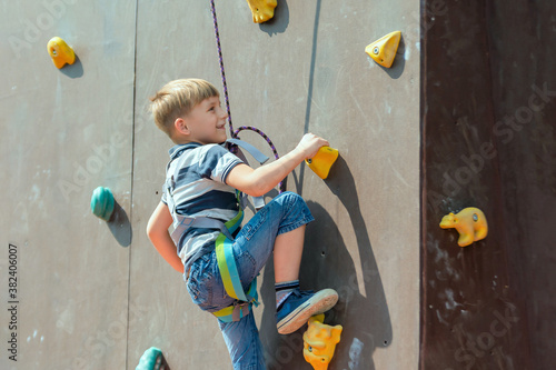 A boy in climbing equipment conquers the top of an artificial to