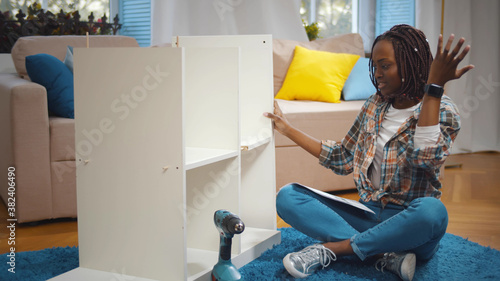 Photos Young african woman with screwdriver and instruction assembling new cupboard at