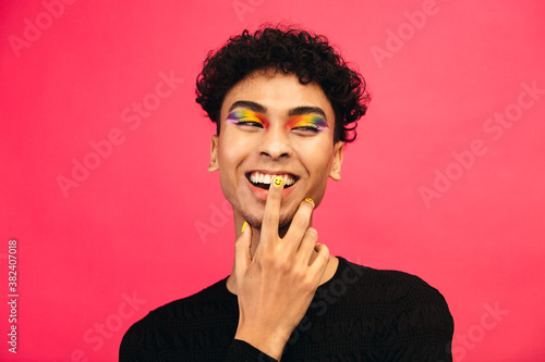 Smiling gay man with rainbow eye shadow and smiley nailpaint photo